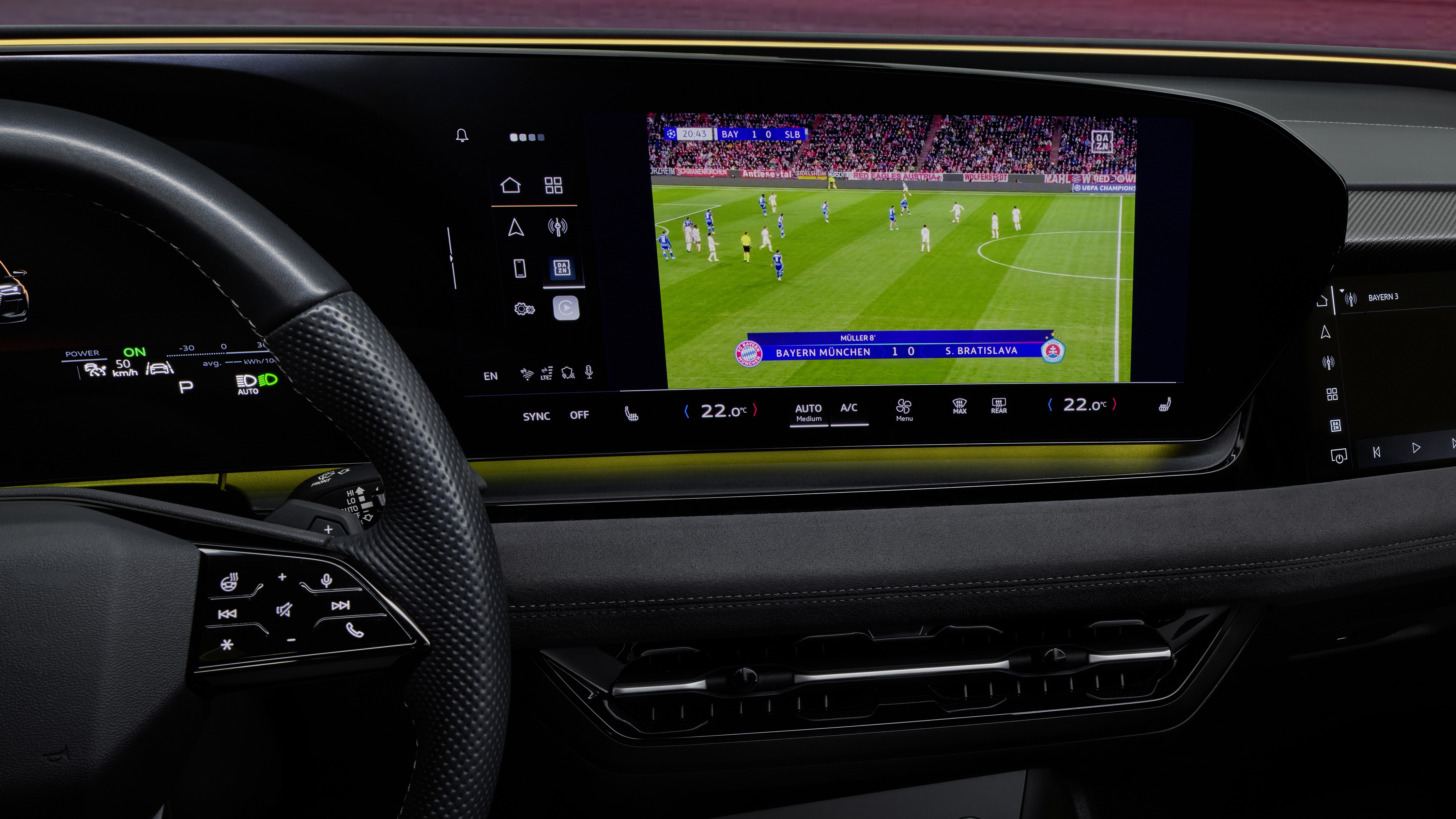 A modern car dashboard displaying a large screen with a live football match featuring Bayern Munich and Slovan Bratislava.