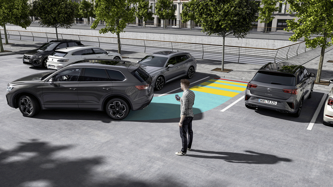 A man uses a smartphone to remotely park a car into a parking space marked with turquoise and yellow lines in an outdoor lot.