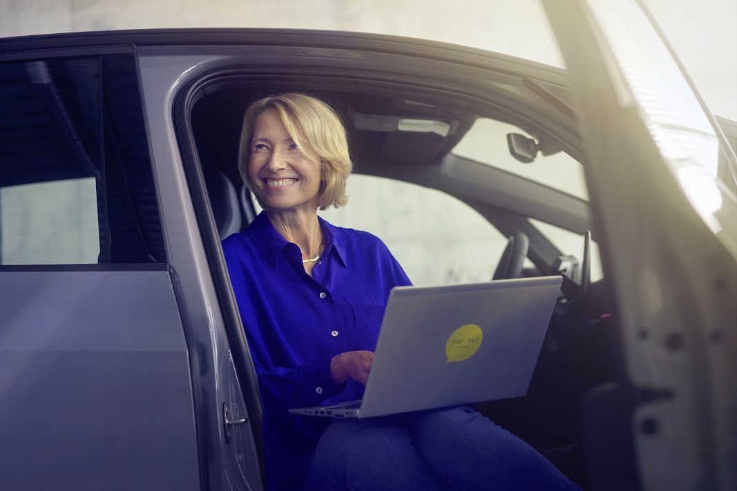smiling-woman-in-blue-blouse-sitting-in-car-door-with-laptop