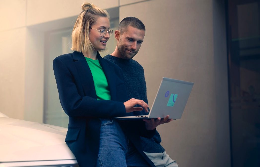 two people with a laptop in front of a car