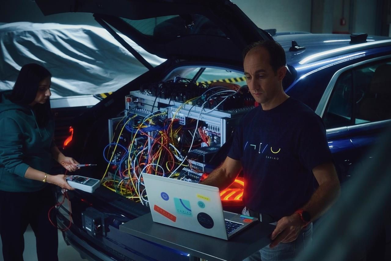 Two individuals collaborate on a high-tech automotive setup, with the car’s trunk revealing intricate electronics and diagnostic tools, highlighting hands-on innovation.