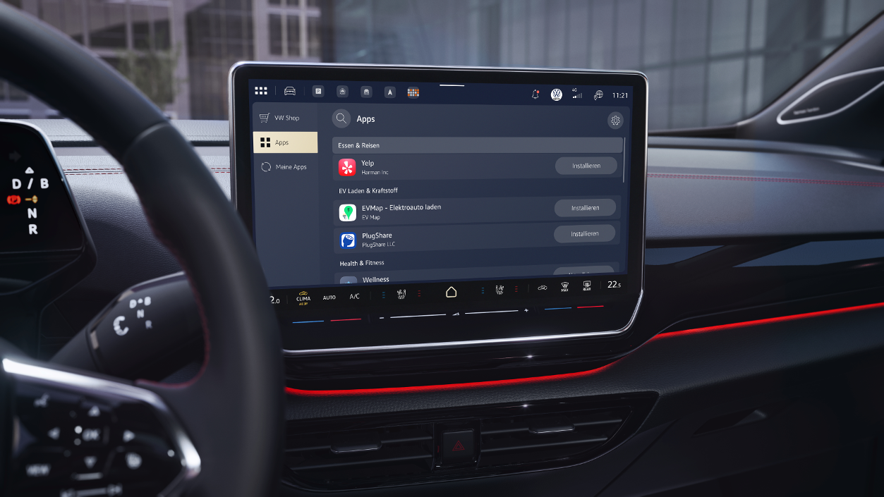 High‑resolution image of a modern Volkswagen vehicle interior featuring a large central touchscreen. The display shows the VW Application Store with a list of available in‑car apps, including Yelp, EV charging services, and wellness applications. The infotainment screen is seamlessly integrated into a premium cockpit with dark surfaces, red ambient lighting, and clearly arranged climate and vehicle controls, highlighting a connected, software‑driven in‑car experience in an urban environment.