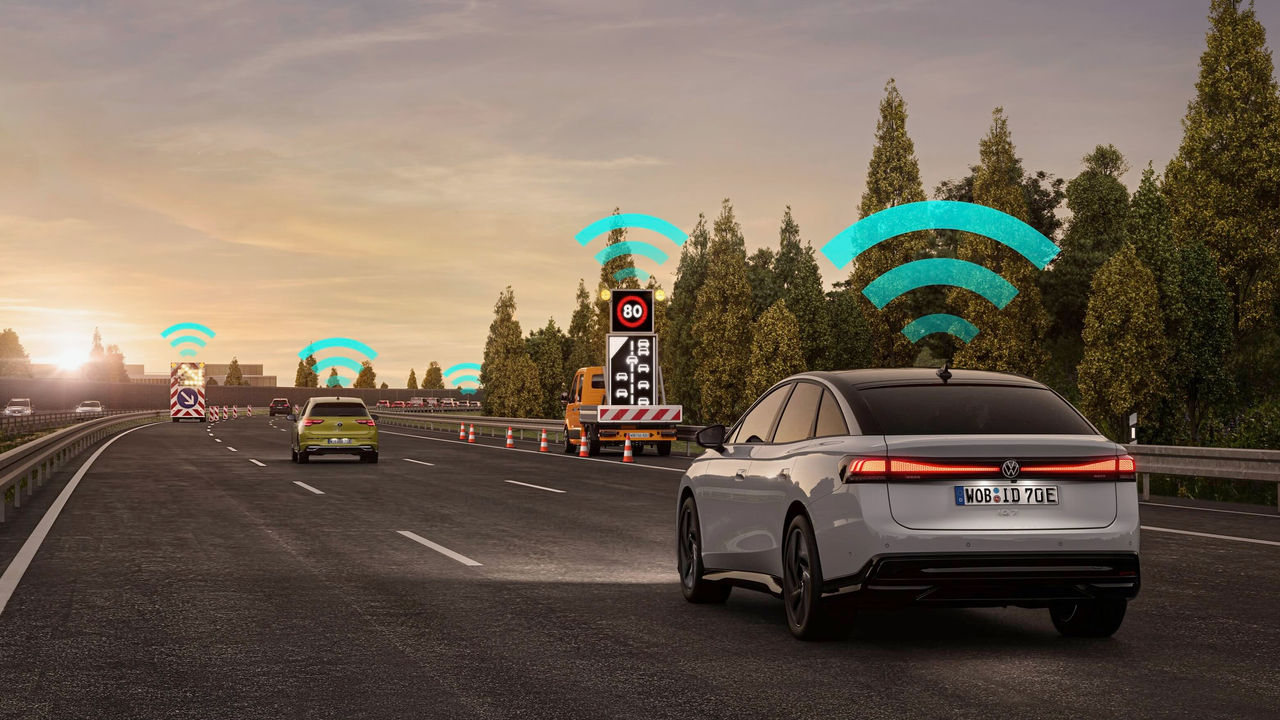 Volkswagen electric vehicle driving on a highway with Car2X communication technology, exchanging data with traffic signs and other cars to enable connected mobility and improve road safety.