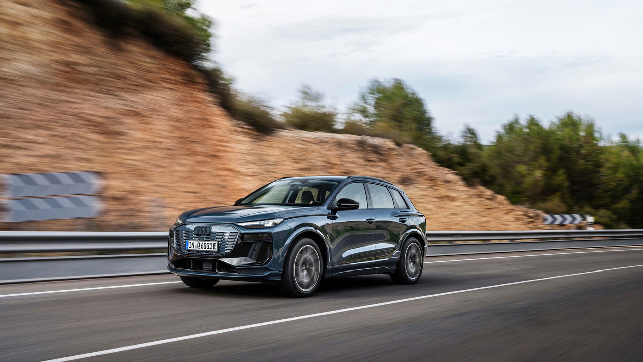 Modern dark SUV driving dynamically on a curved road with guardrails, rocky hillside, and trees in the background.